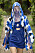 Modell med kort blå klänning med två cutouts vid byster. Över klänningen har modellen en jacka i blått, vitt och svart med luva och tunt tyg framför ansiktet. Look från Kenzo ss21.