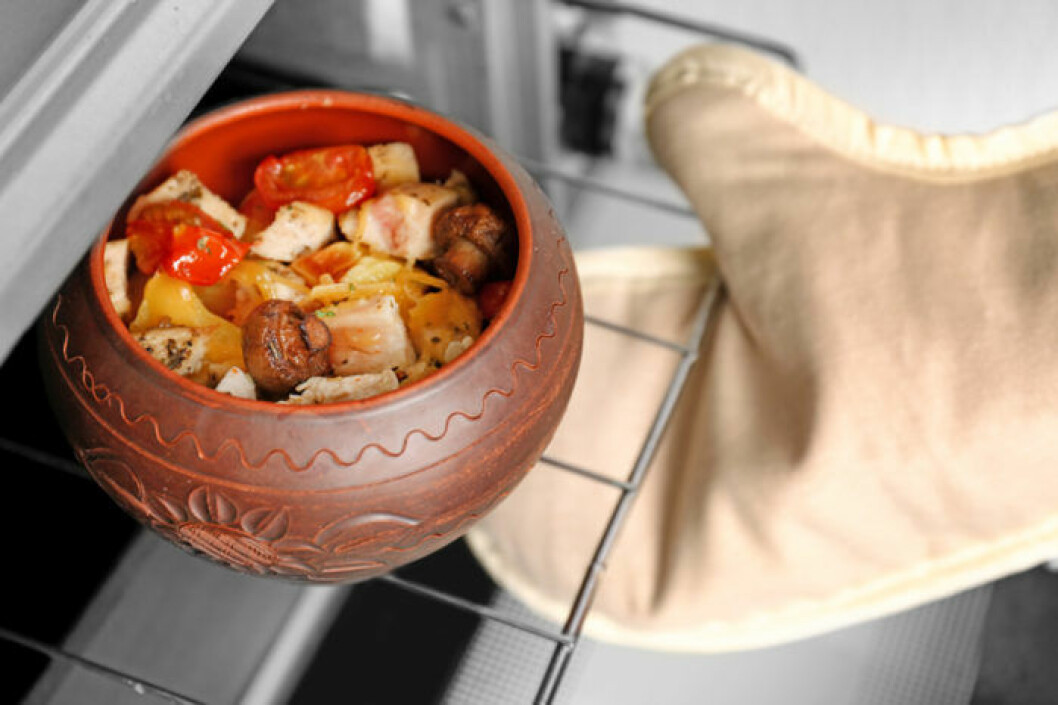 Bild: Shutterstock/IBL Person med grillhandske plockar ut ugnsform som står på galler ur ugn..