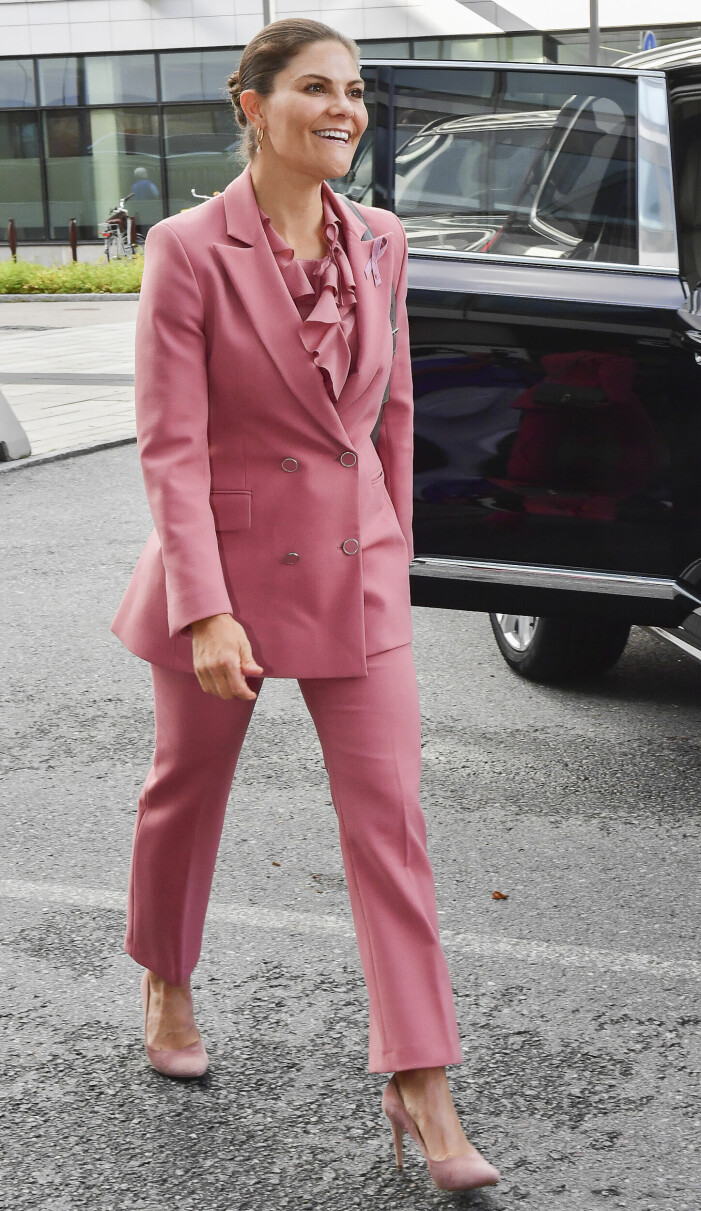Den snygga rosa kostymen matchas med kråsblus och pumps i rosa. Victoria matchar rosa kostym med rosa blus och skor.