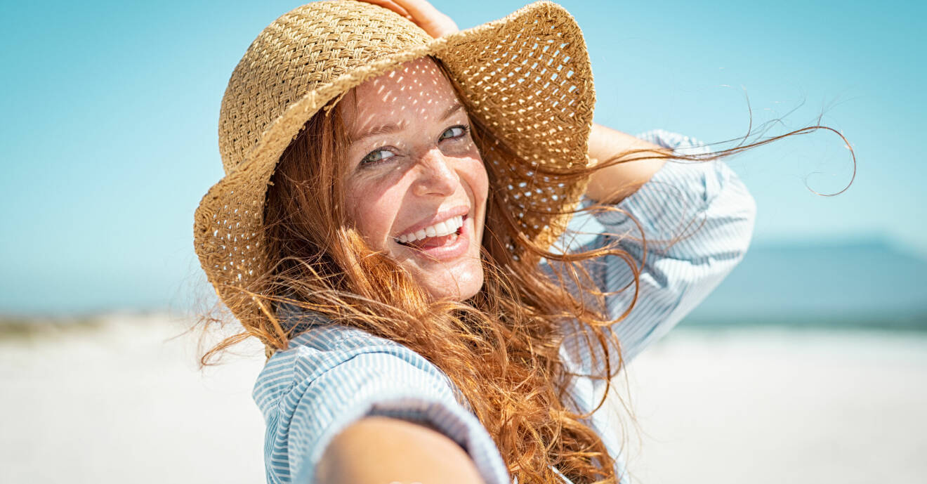 Kvinna på stranden med hatt.