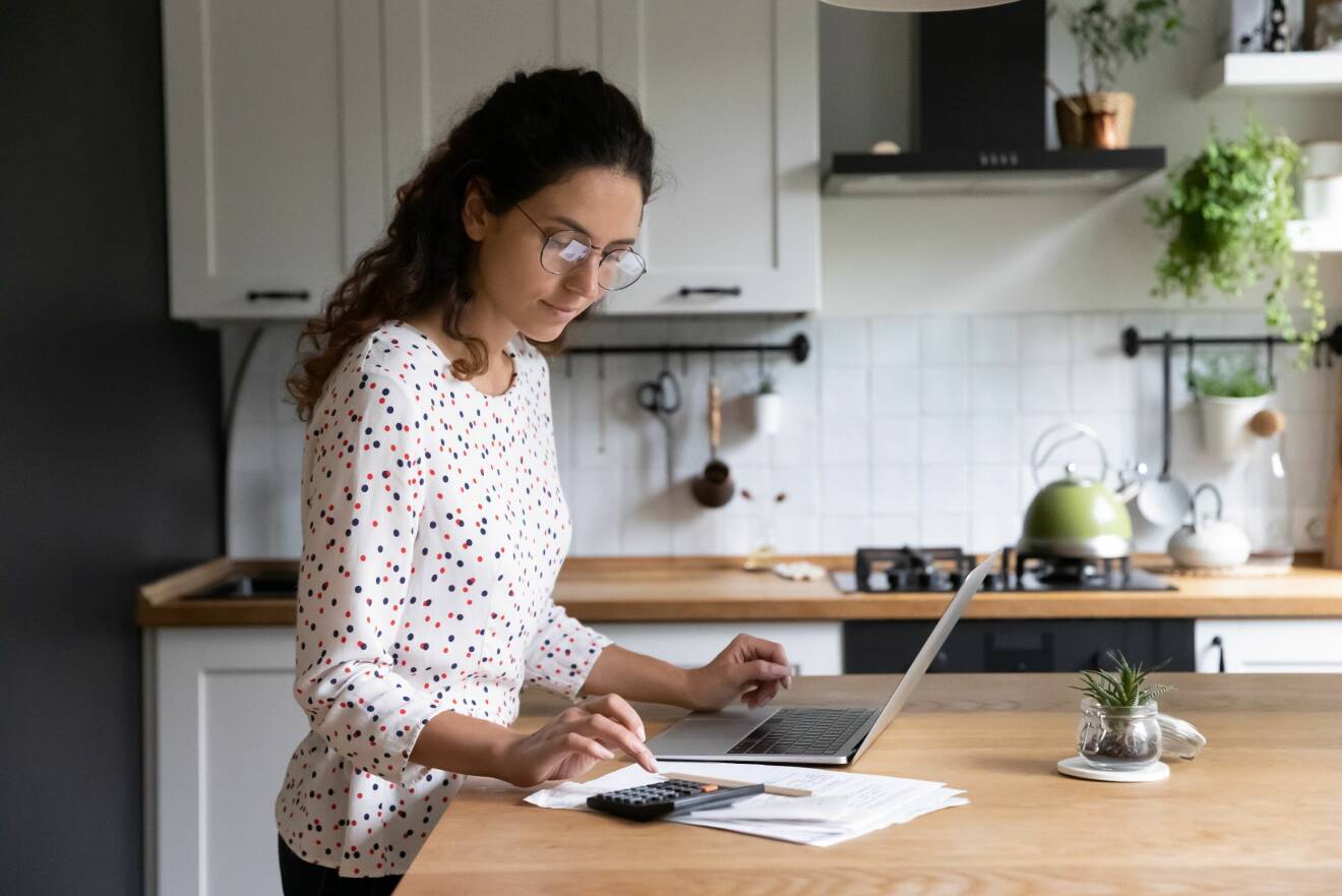 Kvinna står i kök med dator.