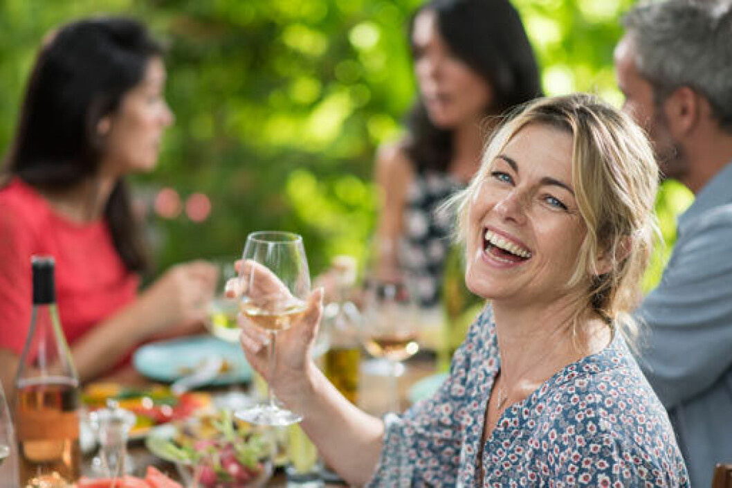 Bild: Shutterstock/IBL Kvinna står utomhus i solen och torkar sig i pannan. I ena handen håller hon en vattenflaska.