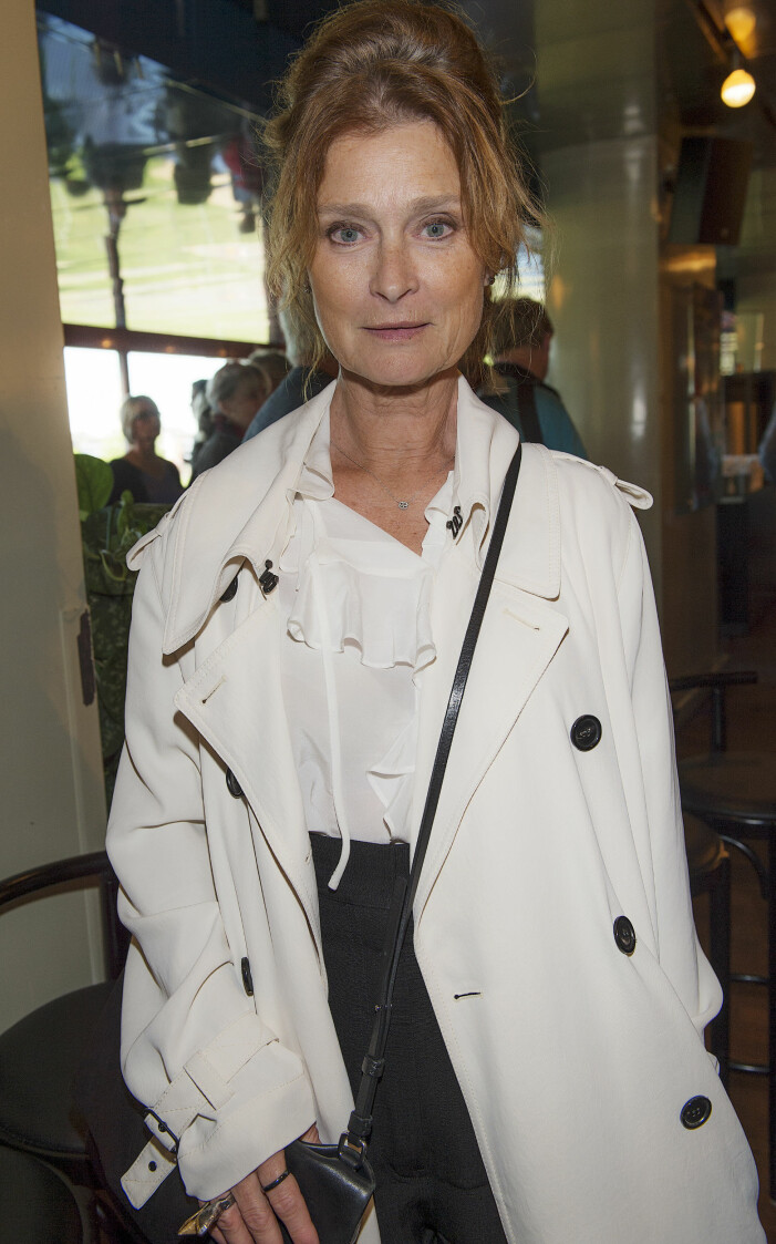 Lena Endre. Foto: TT Lena Endre i uppsatt hår, vit volangblus med en vit trenchcoat över. Svarta byxor med hög midja och en axelremsväska med tunna band över överkroppen.