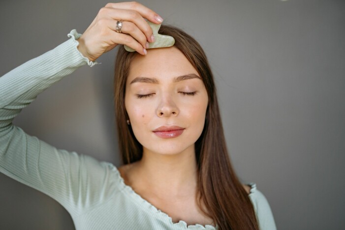 kvinna som masserar sin gua sha i pannan