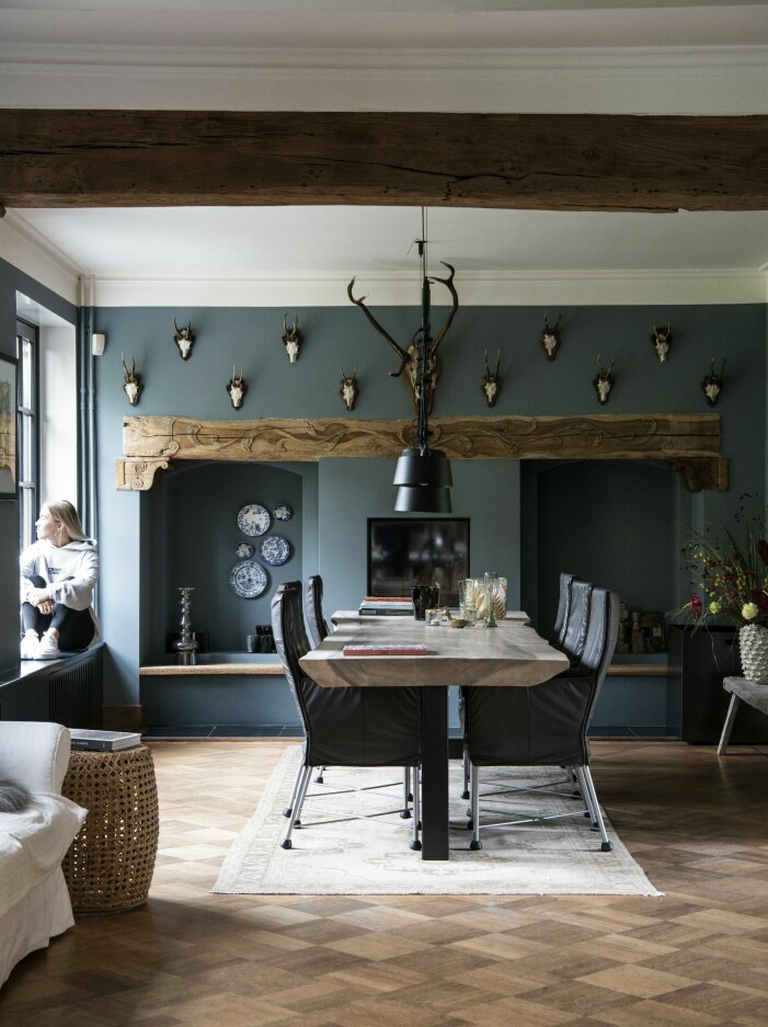 Dottern Pauline sitter uppkrupen i fönstersmygen i matsalen. Matbord, Raw Interiors, stolar, Label, lampa Bolt, Tonone. I prången syns delar av Annemaries samling av blåvitt porslin. Matsal.