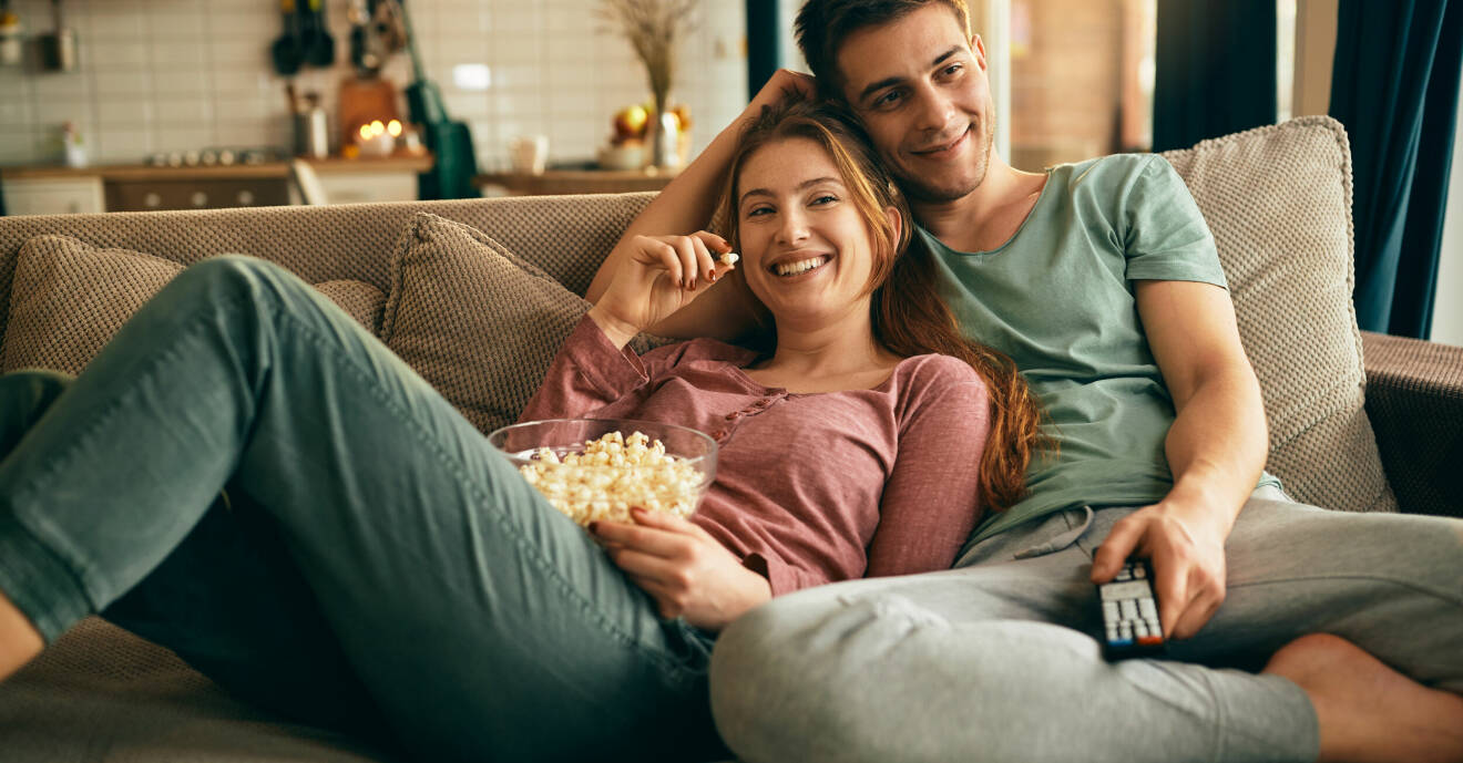 Par sitter i soffan med popcorn och kollar på tv.