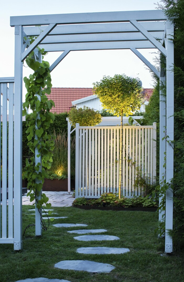 En tydlig port in till den stenlagda trädgårdsdelen, med hemsnickrad portal. Trampstenarna i gräset blir ett naturligt sätt att binda samman den här delen med den övriga trädgården. Port till stenlagd stig.