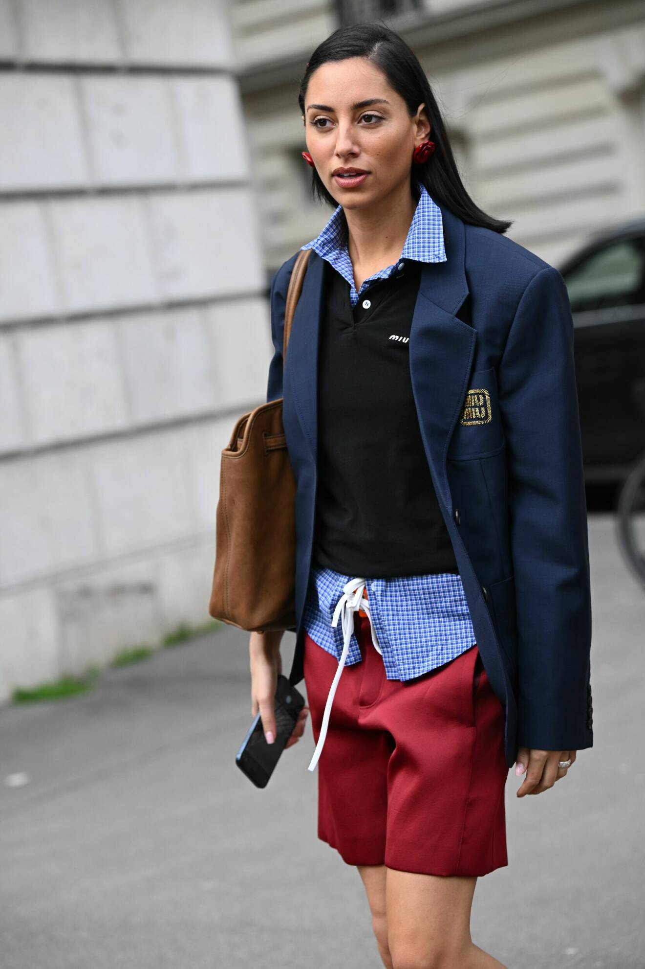 Preppy streetstyle-outfit från Miu Miu med marinblå blazer, rutig skjorta, svart pikétröja och en stor brun mockaväska