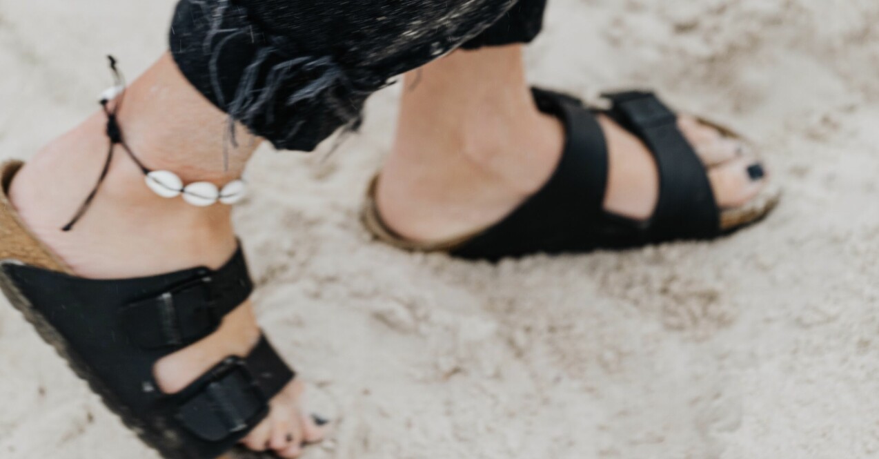 sandalfina fötter i sanden och svart nagellack