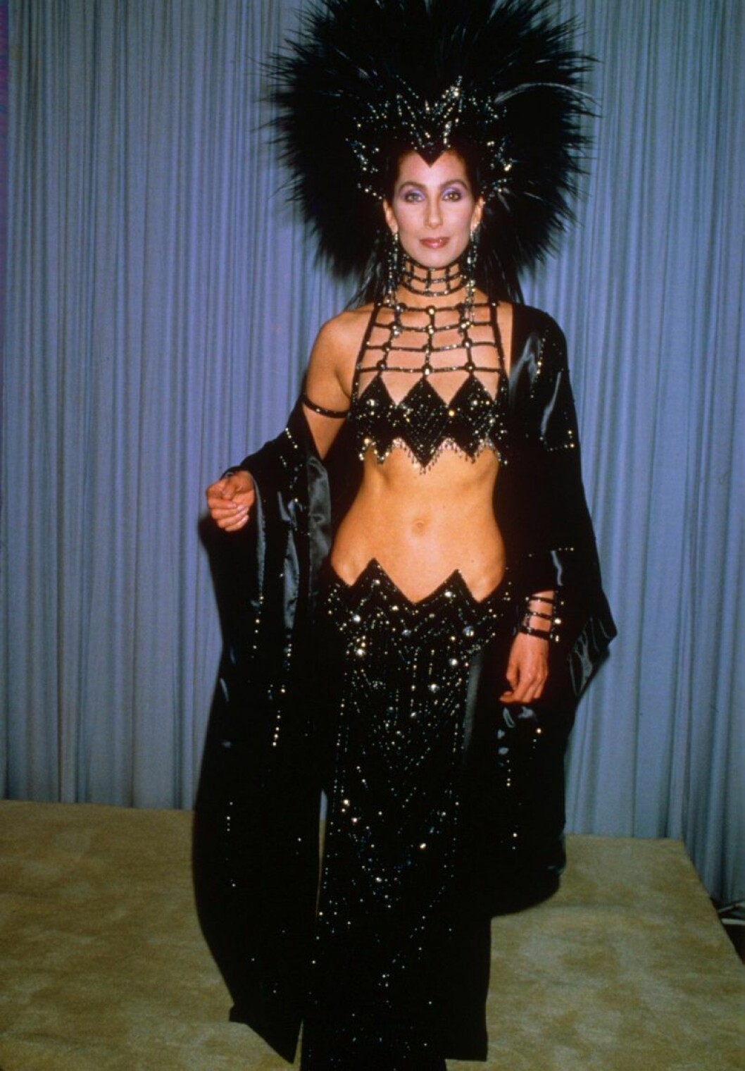 Cher manifesterar i en riktig showgirl outfit. Cher i en svart glittrig showgirl kreation med en stor fjäderdekoration i håret.