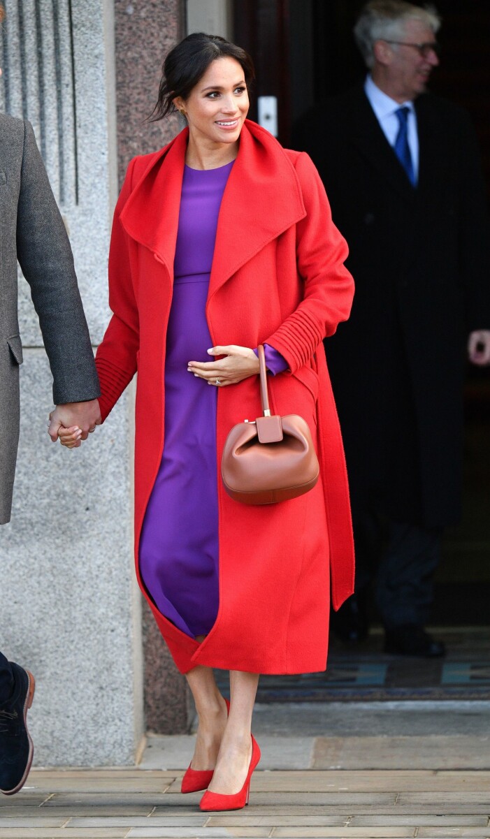 Meghan Markles rock är en del av outfiten och får sitta på hela dagen. Meghan Markle i lila och röd outfit med en röd rock över lila klänning och röda pumps.