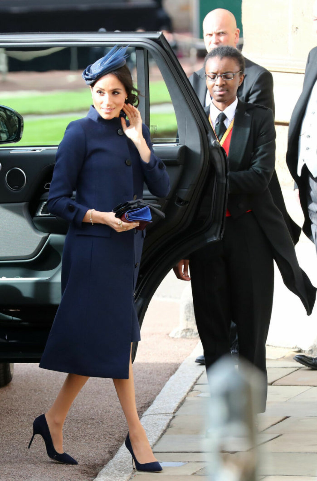 Hertiginnan av Sussex, Meghan anlände i en helt marinblå outfit från Givenchy med matchande liten knappformad hatt. Meghan Markle dolde gravidmagen med en kappa i marinblått.