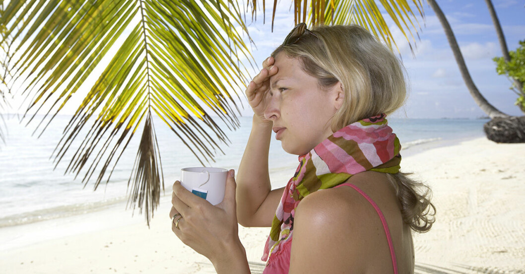 Kvinna under palm på sandstrand håller sig för huvudet och är sjuk