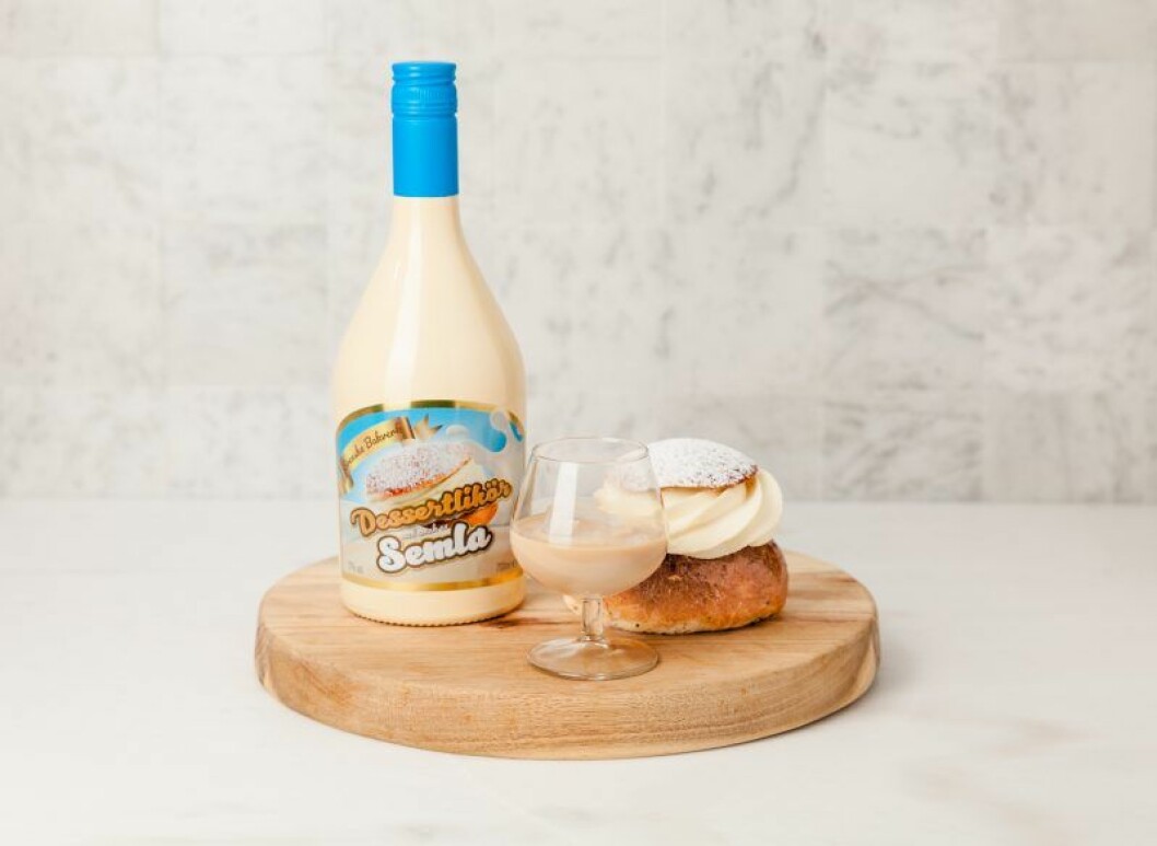 en semla, ett glas med likör och en flaska som står på en rund skärbräda i trä