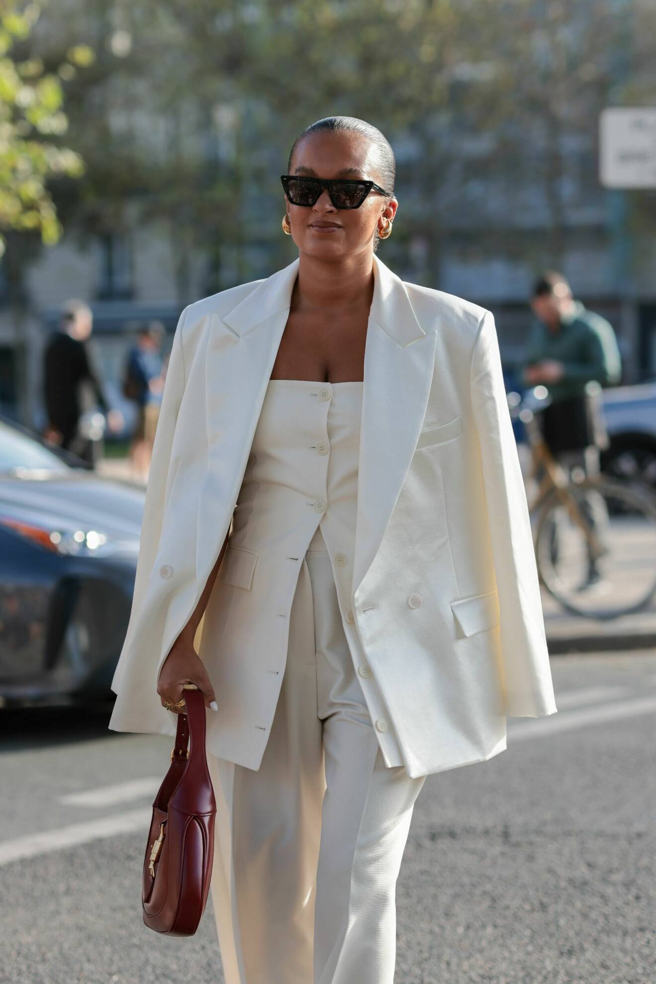 Streetstyleoutfit med vit kostym, guldsmycken och svarta solglasögon