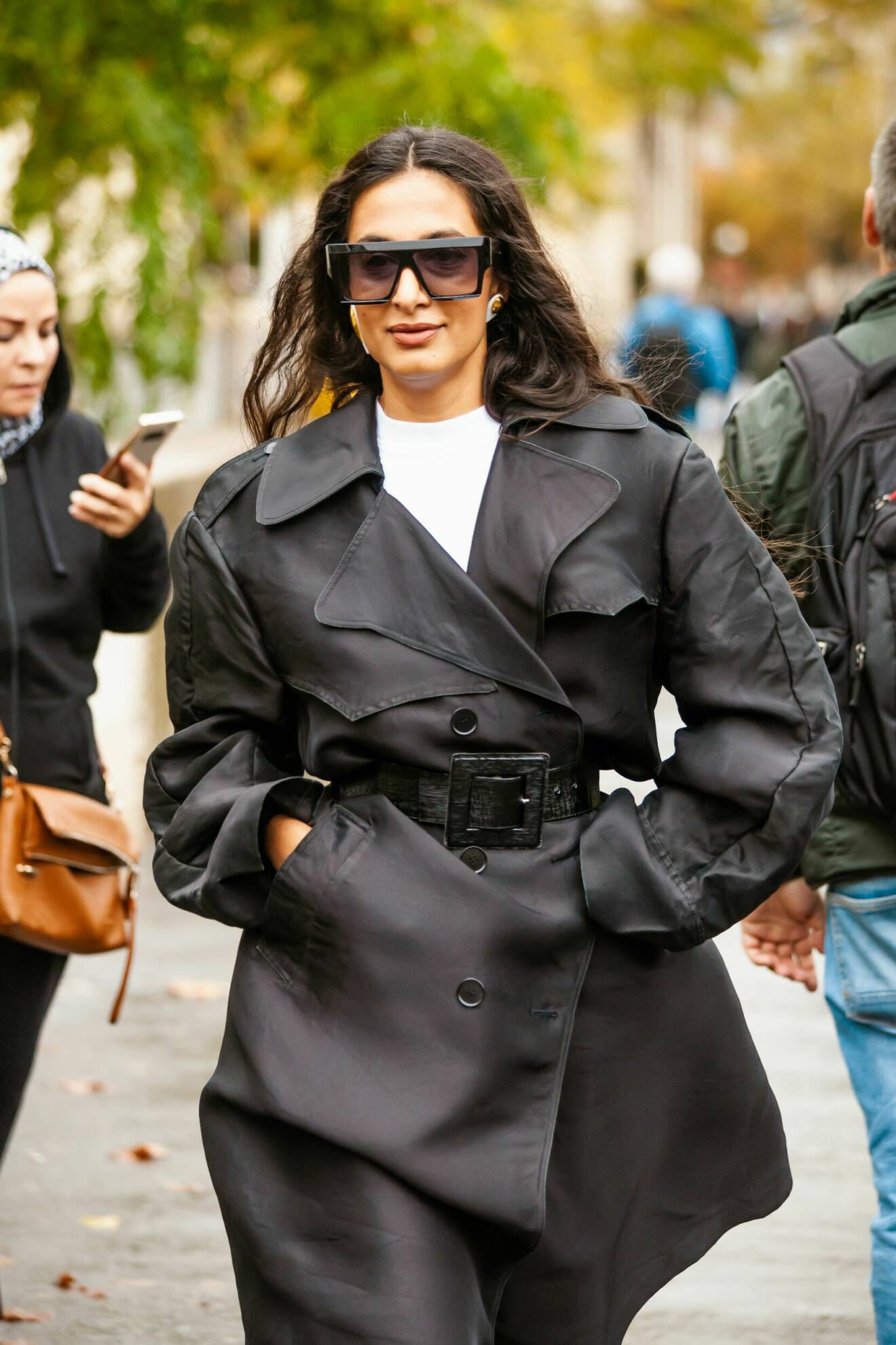 Streetstyle-outfit med svart trenchcoat, svarta solglasögon, vit t-shirt och stora örhängen