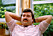 En man med mustasch i rosa skjorta håller händerna bakom huvudet