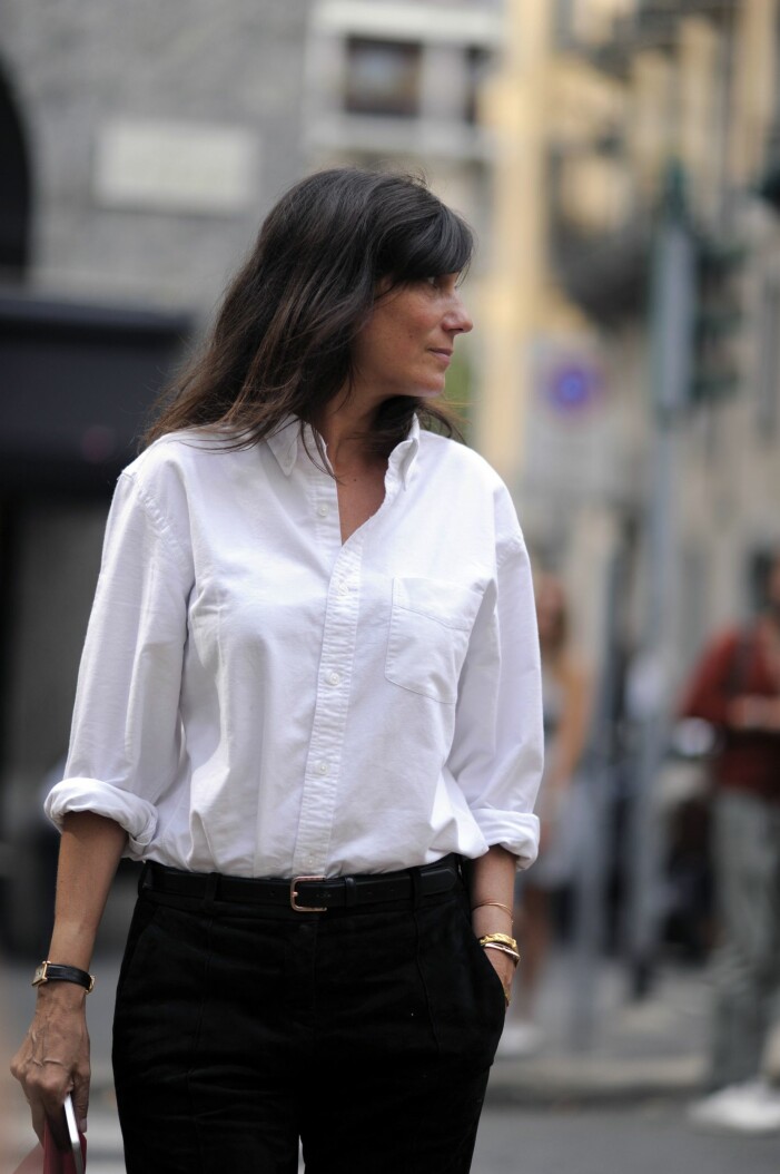 Kvinna i vit, välstruken skjorta i oxfordmodell. Smalt skärp i midjan och svarta jeans.
