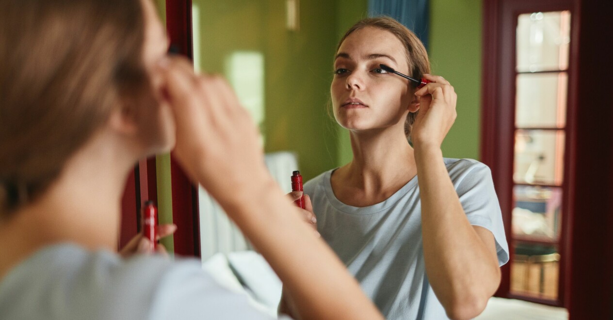 tjej som borstar på mascara framför spegeln