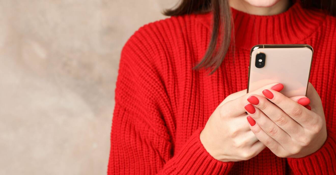 Kvinna i röd tröja som läser på en mobil.