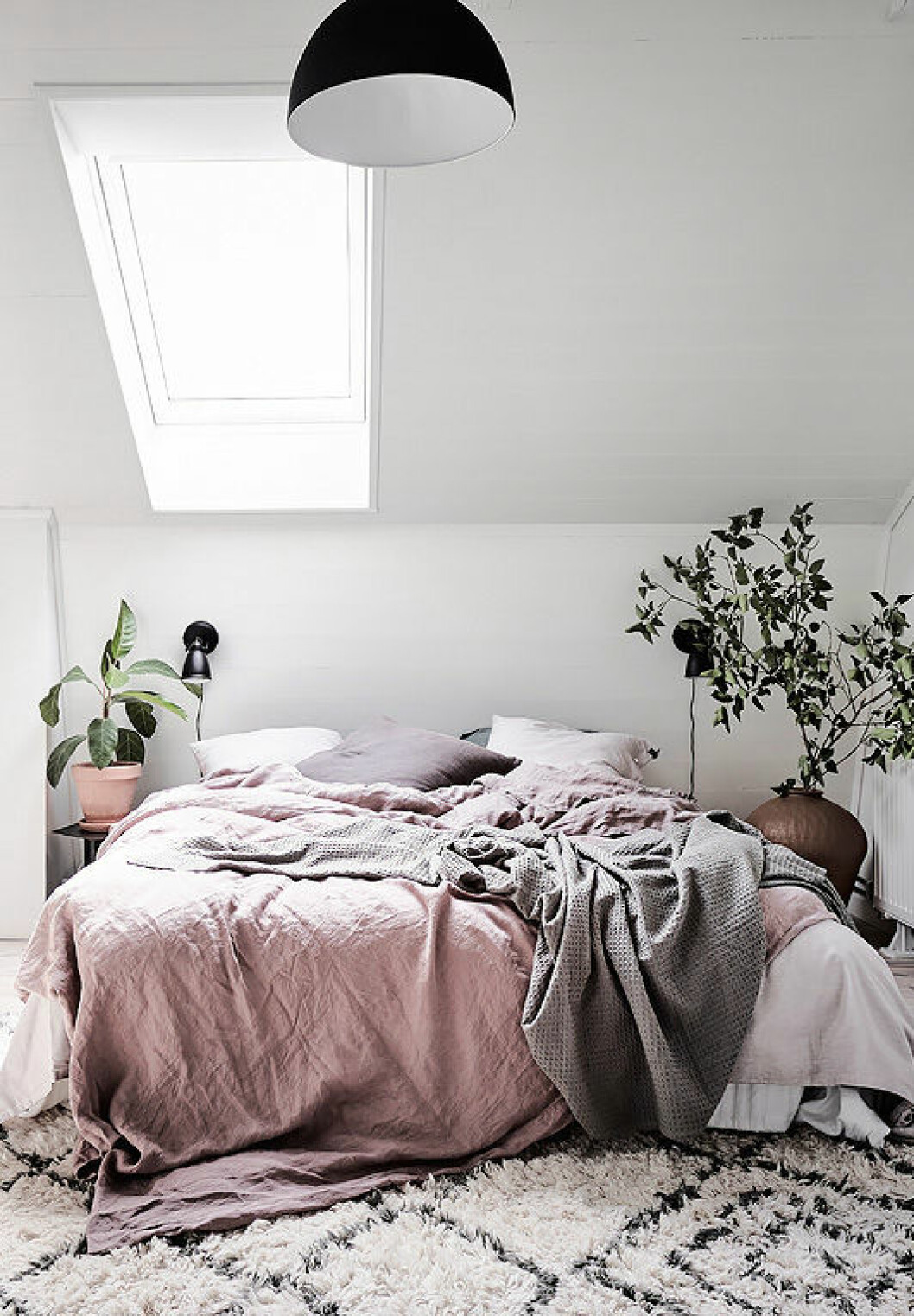 Bedroom with pink linen and green plants.